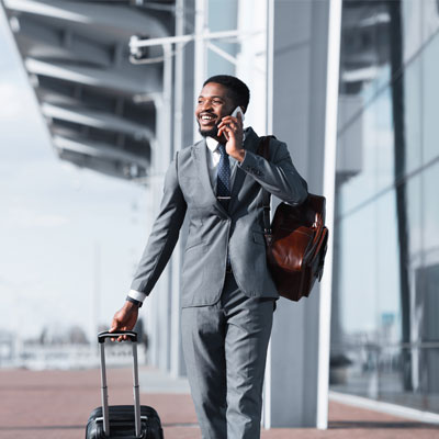 Businessman talking on the phone while walking with a suitcase at the airport.